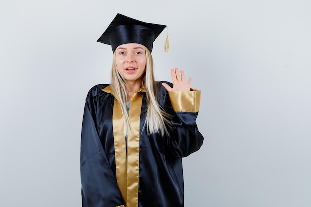 Foto grátis moça mostrando a palma da mão em vestido acadêmico e parecendo feliz.