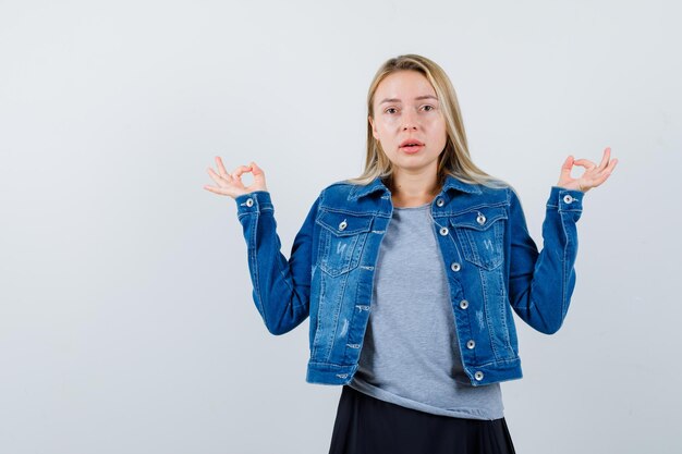 Moça mostrando gesto de ok em camiseta, jaqueta jeans, saia e parecendo confiante