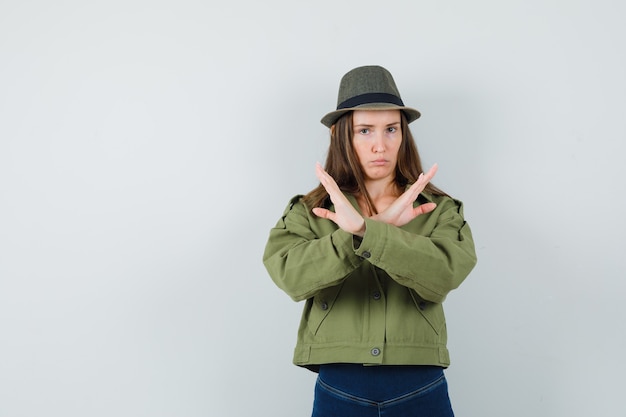 Moça mostrando gesto de pare com chapéu de calça jaqueta e parecendo cansada