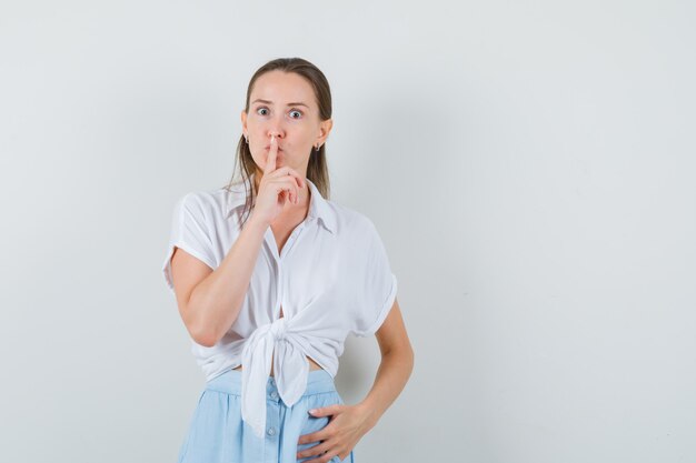 Moça mostrando gesto de silêncio em blusa e saia e parecendo séria