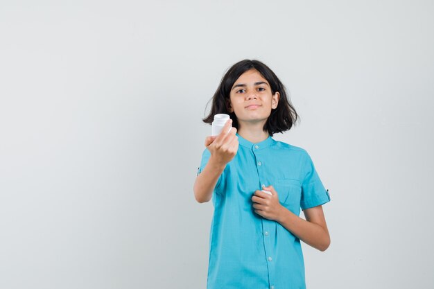 Moça mostrando o frasco de comprimidos na camisa azul e olhando esperançosa.