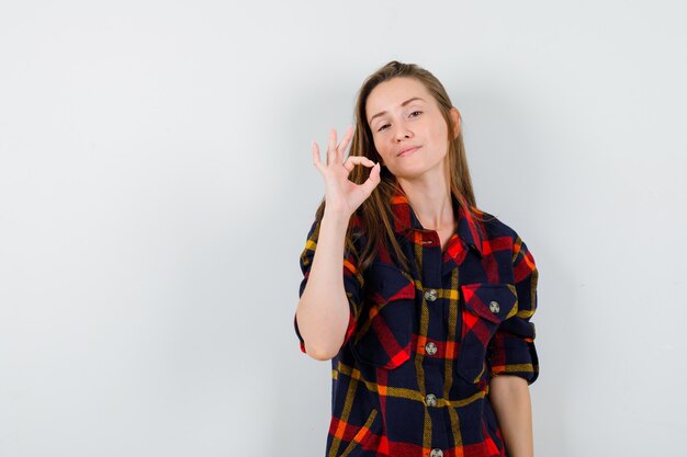 Moça mostrando sinal ok na camisa casual e parecendo orgulhosa. vista frontal.