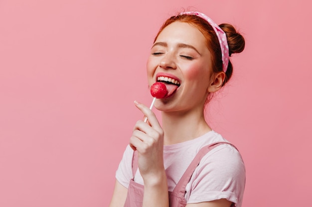 Foto grátis moça na faixa rosa de bom grado lambe pirulito em fundo isolado