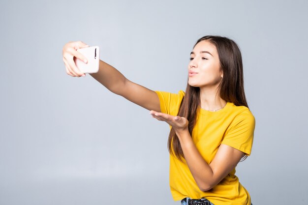 Moça sorridente fazendo foto de selfie em smartphone sobre parede cinza