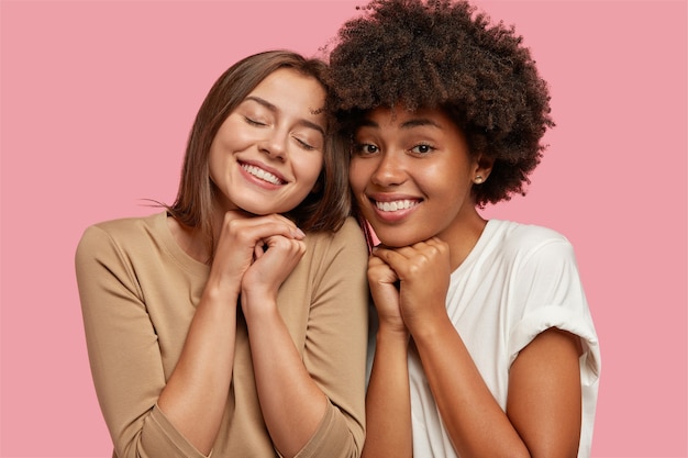 Foto grátis moças ou irmãs inter-raciais sentem proximidade e apoio, têm bons relacionamentos, sorriem com alegria e mantêm as mãos juntas sob o queixo