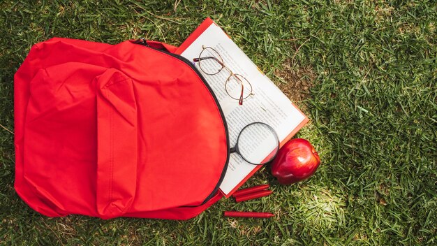 Mochila com livro e óculos na grama