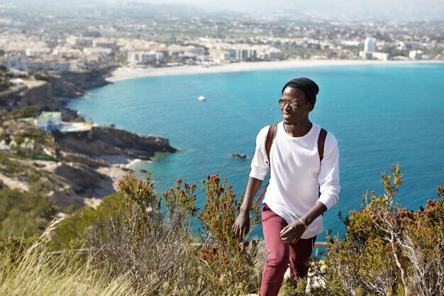 Mochileiro de pele escura atraente vestido casualmente viajando na cidade europeia, voltando da plataforma de visualização