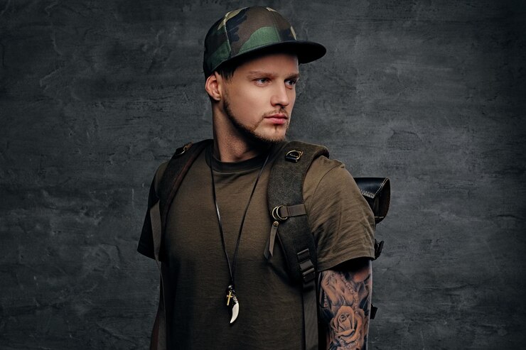 Foto grátis mochileiro estilo urbano com braços tatuados, vestido com camiseta verde escura e boné camo.