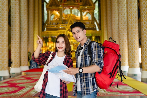 Mochileiros de turista feliz casal asiático segurando o mapa de papel e procurando direção enquanto viajava no templo tailandês de férias na tailândia, uma linda mulher apontando o alvo.