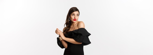 Foto grátis moda e beleza jovem boba de vestido preto fazendo beicinho e parecendo tímida em pé no glam preto