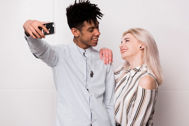 Foto grátis moda jovem interracial sorridente casal tendo selfie em smartphone