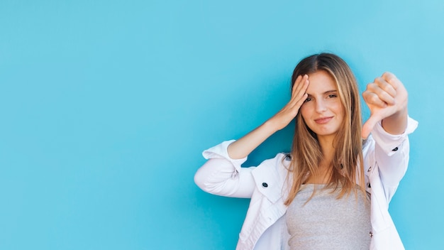 Foto grátis moda jovem mostrando os polegares para baixo contra o pano de fundo azul