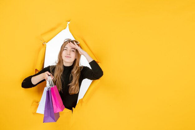 Moda jovem mulher com sacolas de compras através de um buraco de papel rasgado na parede