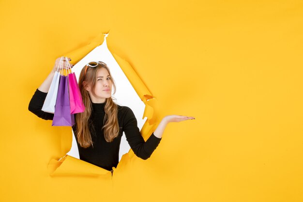 Moda jovem mulher com sacolas de compras através de um buraco de papel rasgado na parede