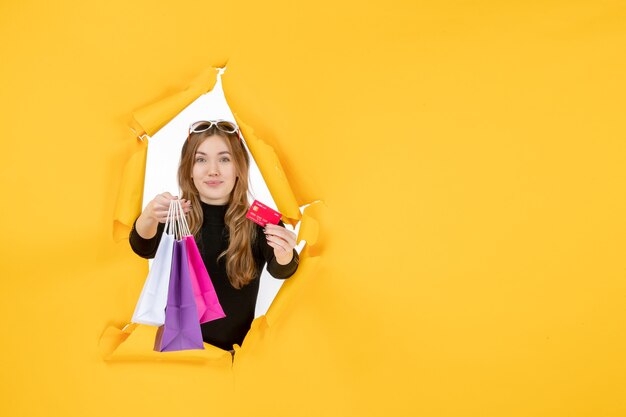 Moda jovem segurando sacolas de compras e cartão de crédito pelo buraco de papel rasgado na parede