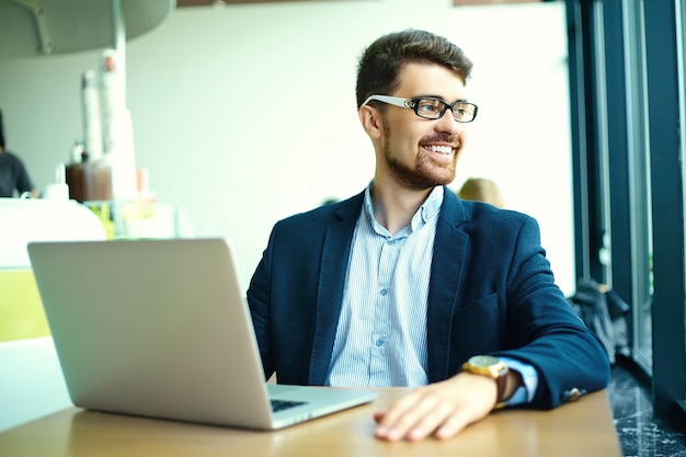 Moda jovem sorridente homem hipster no café da cidade durante a hora do almoço com o notebook no terno