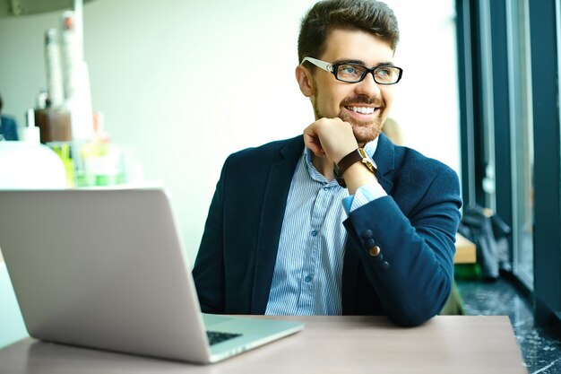 Moda jovem sorridente homem hipster no café da cidade durante a hora do almoço com o notebook no terno