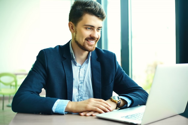 Moda jovem sorridente homem hipster no café da cidade durante a hora do almoço com o notebook no terno