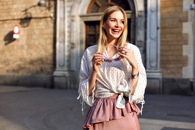 Moda luxo retrato ensolarado de mulher loira posando na rua usando blusa e saia longa de seda