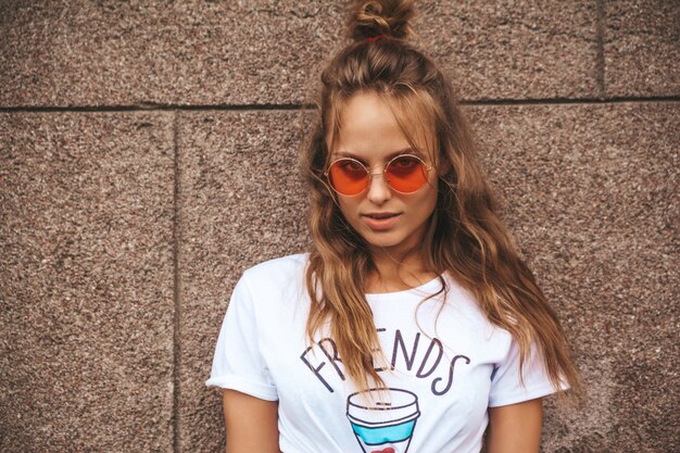 Foto grátis modelo adolescente bonito loiro bonito em roupas de hipster branco verão posando perto da parede na rua