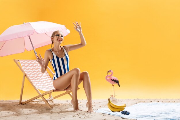 Modelo bonito em roupas de praia posa acenando a mão e sorrindo