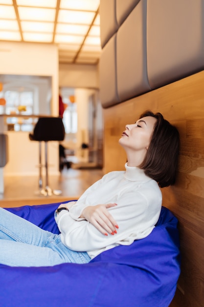 Modelo de cabelos curtos sexy descansar e tirar uma soneca diária sentado na cadeira saco azul em casa