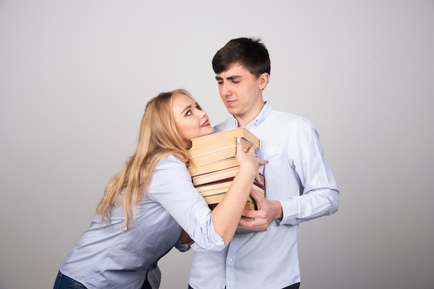 Modelo de cara morena de pé e carregando uma pilha de livros perto de uma mulher loira