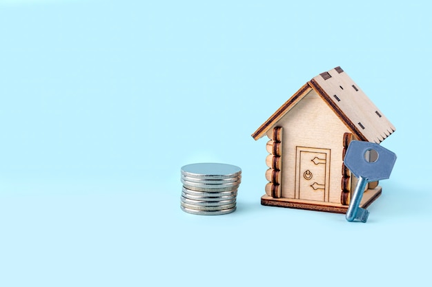 Modelo de casa de madeira, estoca dinheiro e chave sobre fundo azul. conceito de compra e venda de casas e imóveis. seguro residencial, propriedade e hipoteca. copie o espaço para o texto