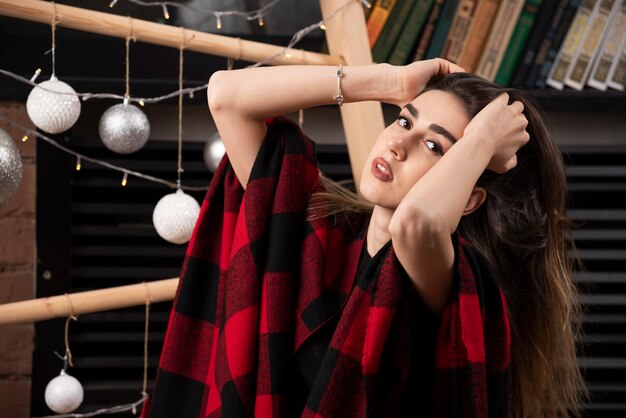 Modelo de jovem posando com manta quadriculada perto de bolas de Natal.