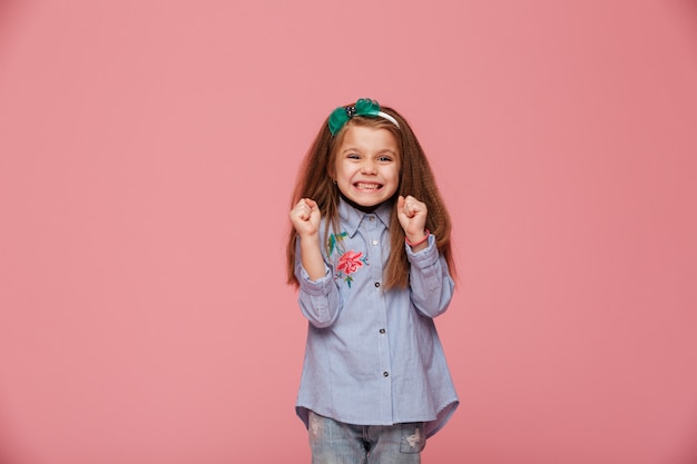 Modelo de menina sorridente em aro de cabelo e roupas da moda, expressando a felicidade gesticulando com os punhos cerrados