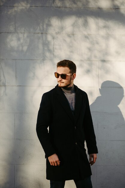 Modelo de moda jovem bonito posando nas ruas da cidade. Retrato de moda ao ar livre, homem elegante com casaco elegante.