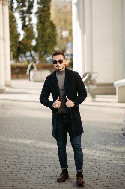Modelo de moda jovem bonito posando nas ruas da cidade. Retrato de moda ao ar livre, homem elegante com casaco elegante.