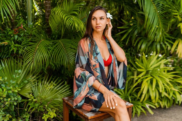 Modelo de mulher graciosa em roupa de banho vermelha com cabelo longo e reto, posando na natureza tropical.