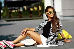 Foto grátis modelo elegante mulher jovem e bonita morena em roupas casuais coloridas de hipster de verão posando na rua fundo