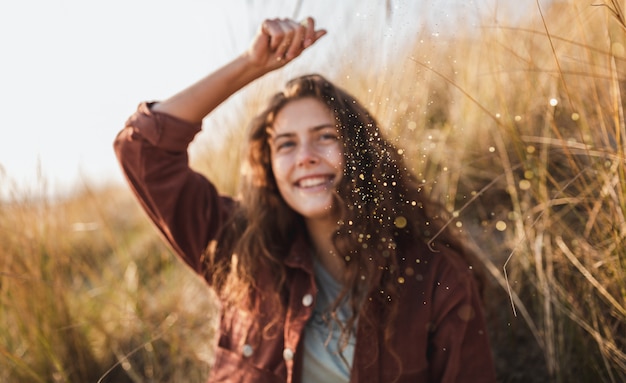 Modelo encaracolado em uma jaqueta marrom sorrindo e jogando glitter no ar