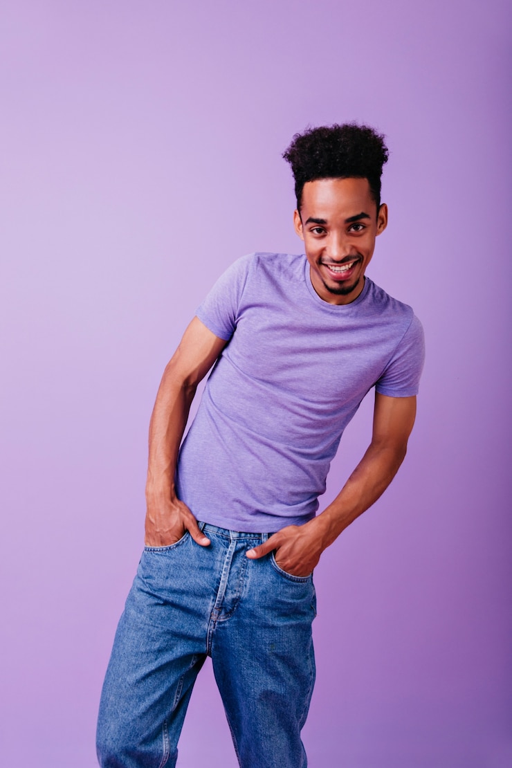 Foto grátis modelo engraçado feliz em pé com as mãos nos bolsos e sorrindo. despreocupado cara africano com cabelo encaracolado, expressando interesse.