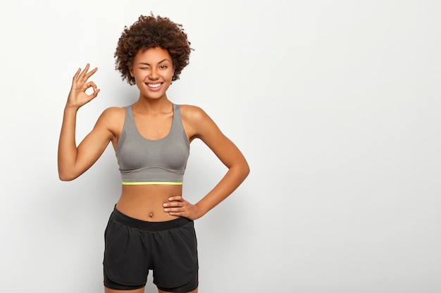 Foto grátis modelo esportivo em roupas esportivas mostra bom gesto com a mão, garante que está tudo bem, mantém a outra mão na cintura