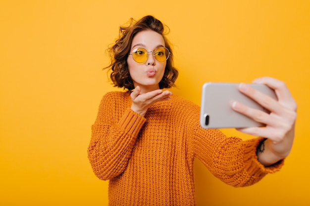 Modelo feminina encantadora mandando beijo no ar enquanto faz selfie