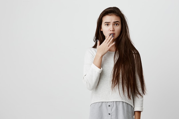 Modelo feminina espantada e chocada, com cabelos escuros lisos, vestindo roupas casuais, olhando com olhos esbugalhados e perplexidade, atordoada e assustada por causa das notícias que ouviu.