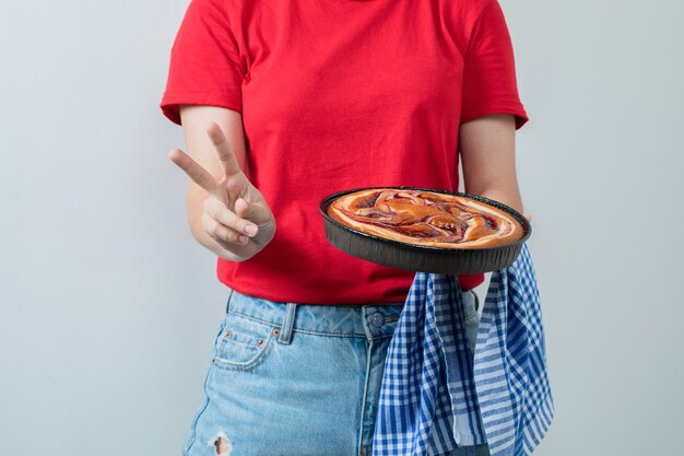 Modelo feminino de camisa vermelha, segurando uma torta doce em uma panela preta.