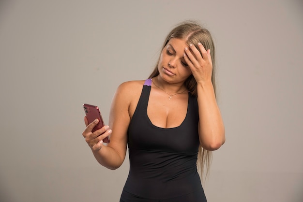 Modelo feminino em mensagens de texto de sutiã esporte com seu smartphone e parece cansado.
