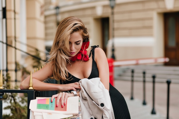 Modelo feminino europeu cansado olhando para o relógio de pulso enquanto espera alguém no beco em um lindo traje