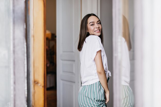 Modelo feminino inspirado em t-shirt branca relaxante na manhã de fim de semana. Retrato interior de sorridente senhora caucasiana usa roupas da moda em casa.