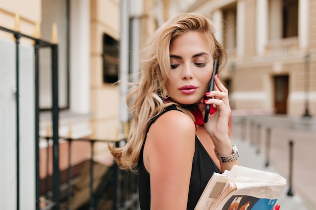 Modelo feminino levemente bronzeado com longos cabelos loiros ouvindo alguém no telefone com os olhos fechados