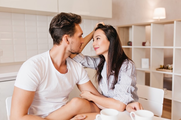 Modelo feminino romântico com cabelo liso olhando para o marido com ternura após o café da manhã