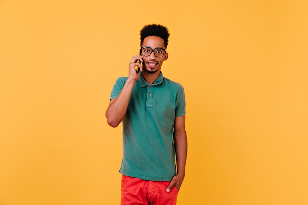 Modelo masculino preto surpreso, falando no telefone. cara africano elegante em copos posando com smartphone.