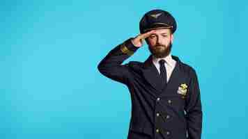 Foto grátis modelo masculino vestindo uniforme de piloto e chapéu na câmera, tendo ocupação profissional na companhia aérea. jovem trabalhando como capitão e avião voador, sendo feliz e positivo no estúdio.