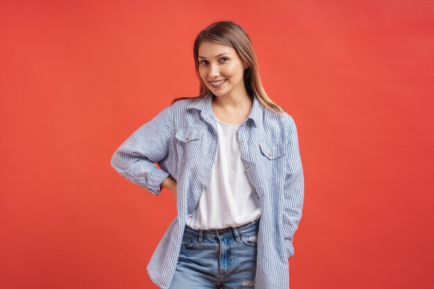 Modelo muito feminino, posando com uma expressão de rosto sorridente na parede vermelha