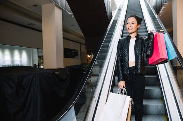 Modelo na moda com sacos posando em escada rolante