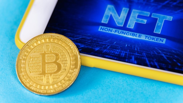 Moeda de ouro física bitcoin e smartphone com nft nele fundo azul